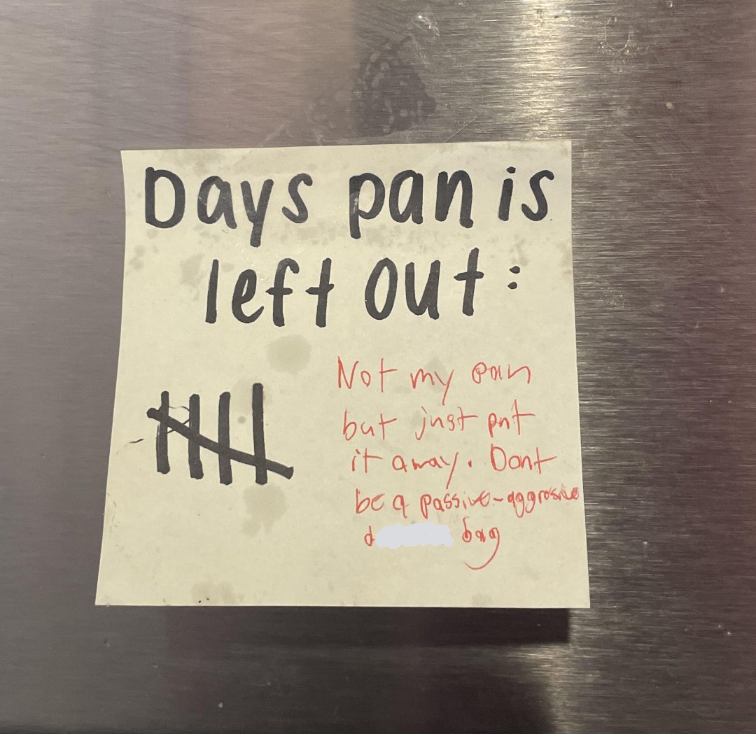 A sticky note on a metallic surface reads "Days pan is left out:" with five tally marks. In red, it says, "Not my pan but just put it away! Don’t be a passive-aggressive [word obscured].