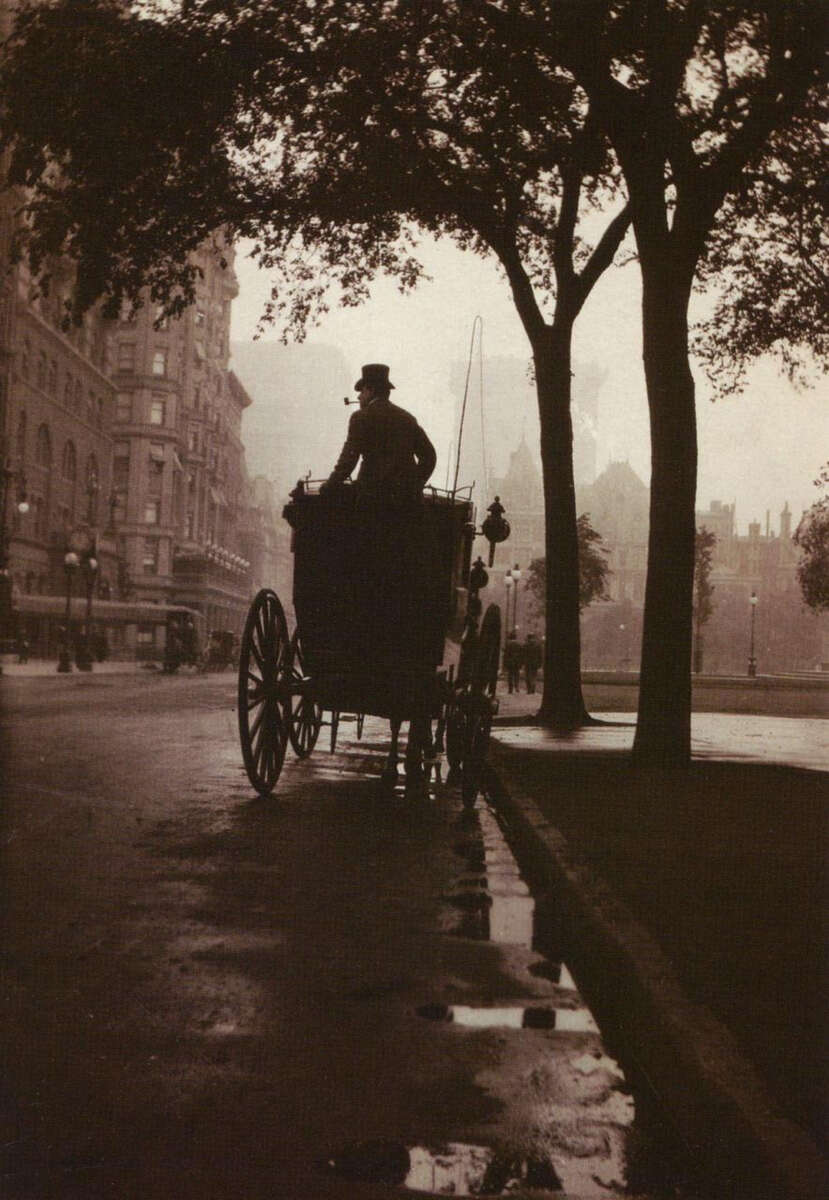 A silhouette of a horse-drawn carriage with a driver in a top hat travels down a wet, tree-lined city street at dusk; surrounding buildings fade into the misty background.
