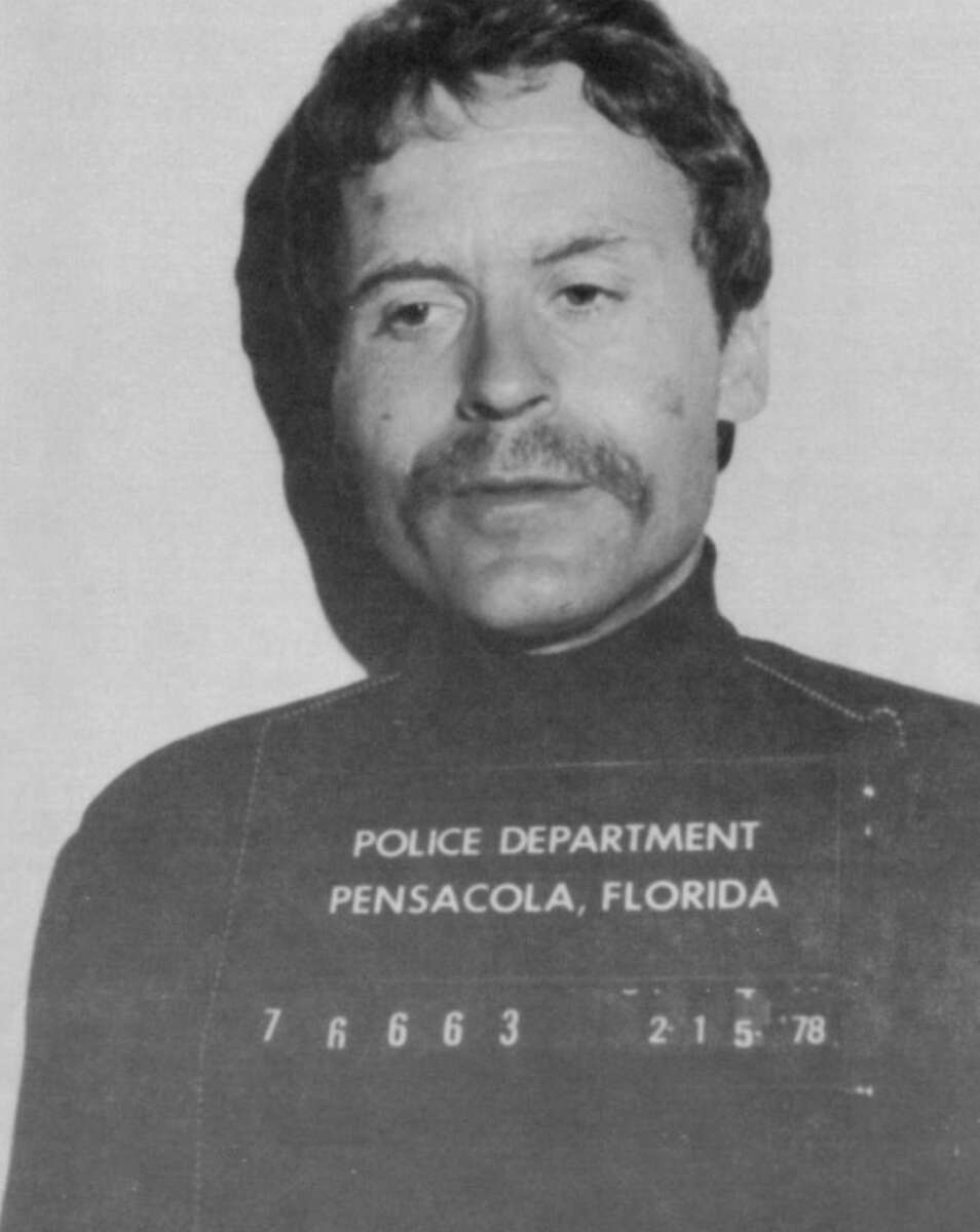 Black and white mugshot of a man with a mustache, wearing a dark shirt. The sign reads "Police Department Pensacola, Florida" with identification numbers and the date 2-15-78.