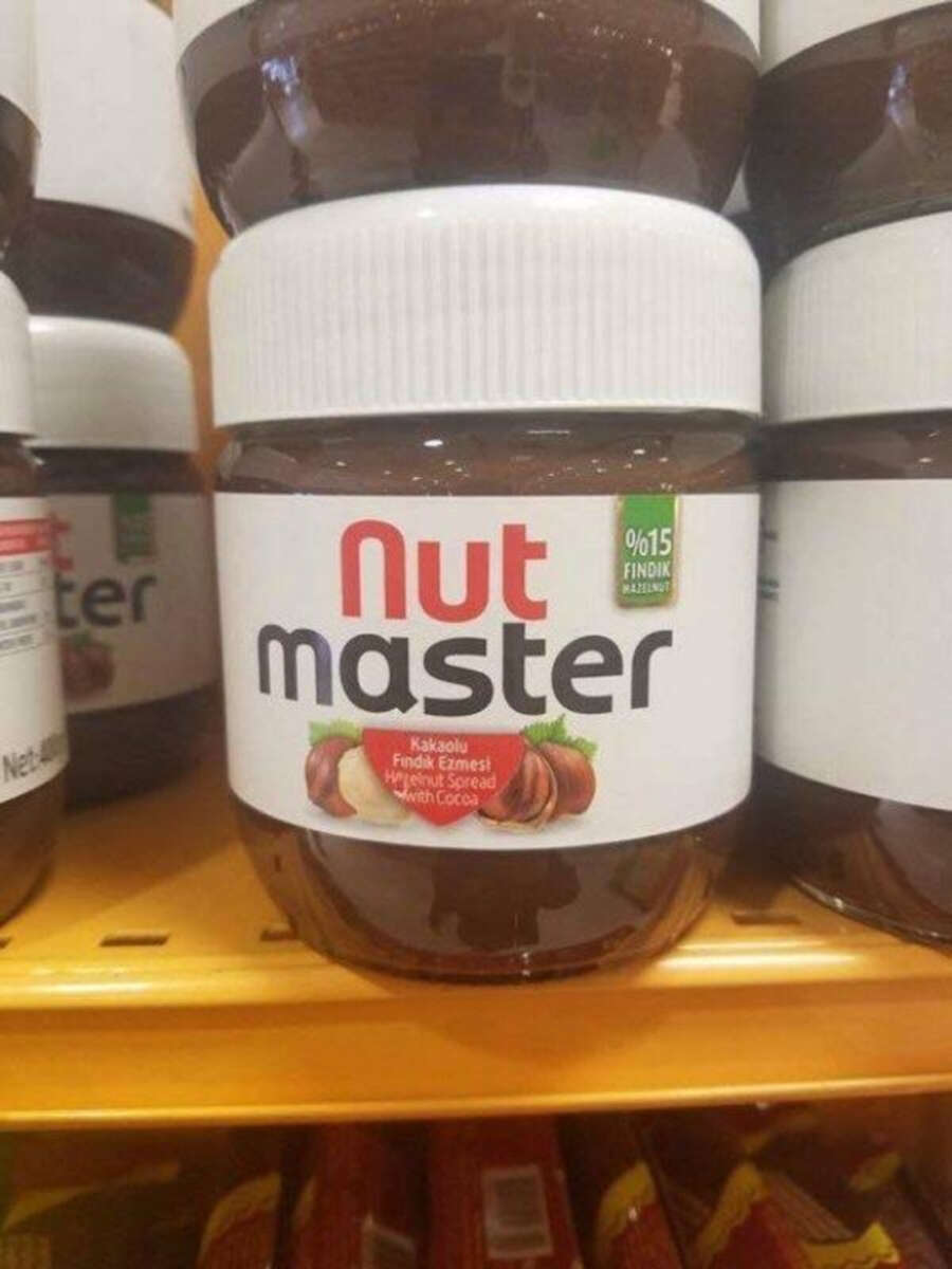 A jar labeled "Nut master" hazelnut spread with cocoa, featuring an image of hazelnuts, sits on a yellow store shelf next to other similar jars.