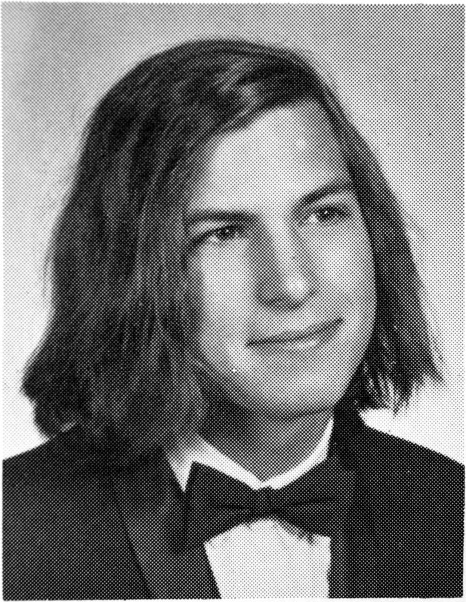 Black-and-white yearbook-style portrait of a young person with long hair, wearing a tuxedo with a bow tie, looking slightly to the side and smiling softly.