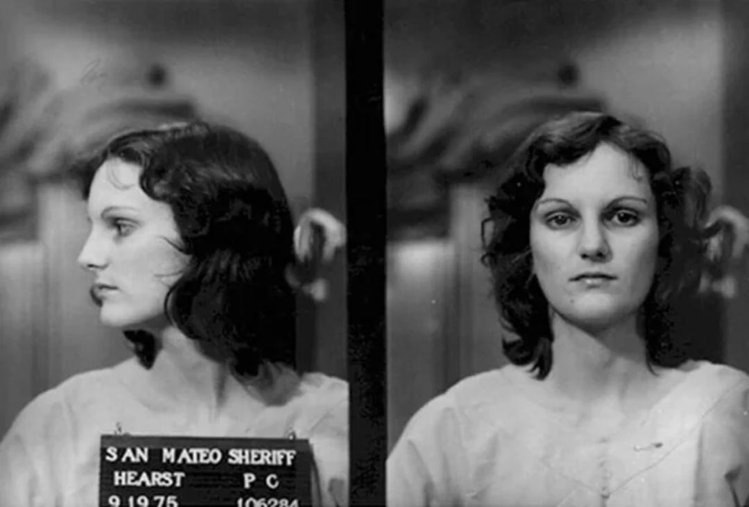 Black and white mugshot photo of a young woman with wavy dark hair, shown in both profile and front view. She wears a light-colored top and holds a placard that reads "San Mateo Sheriff" with other details.