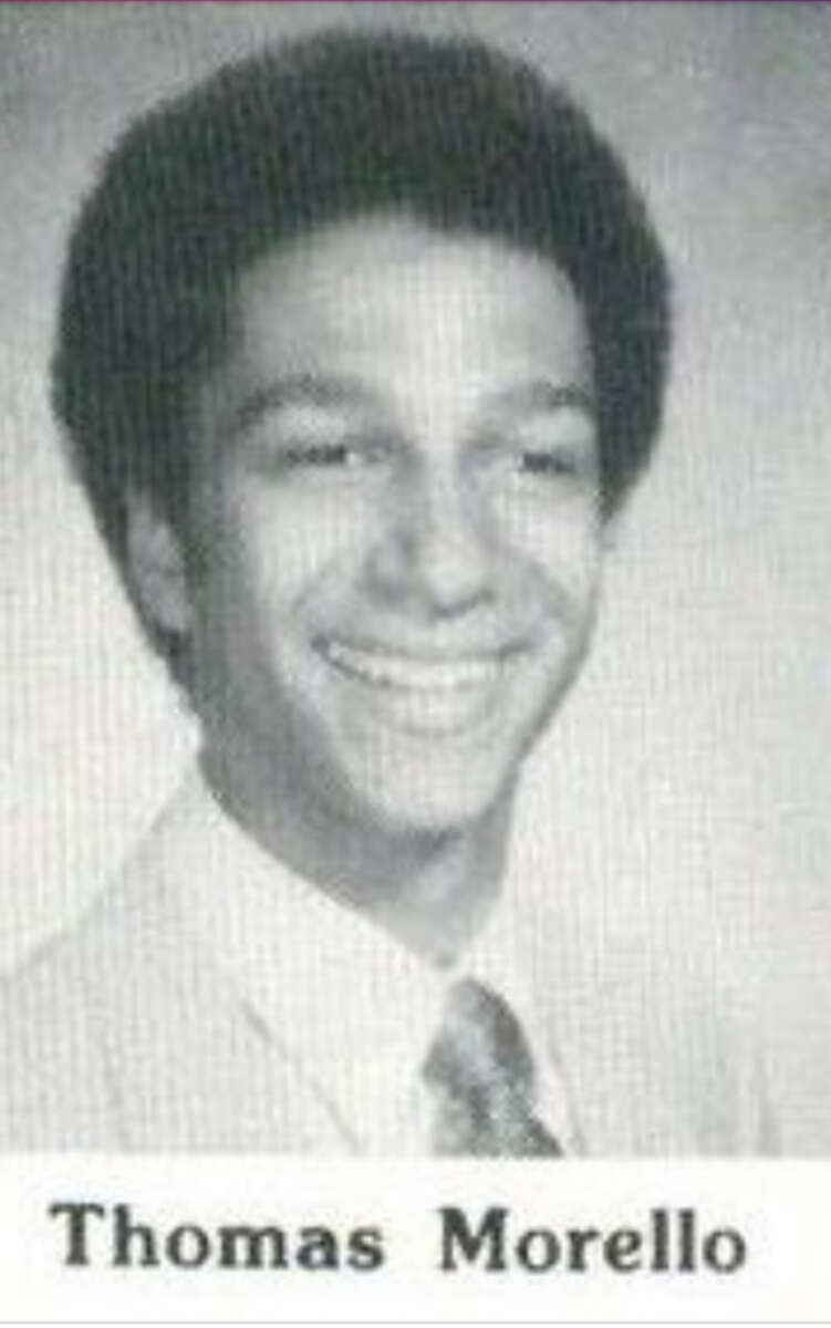 Black-and-white yearbook photo of a young man with short curly hair, smiling, wearing a light-colored suit, shirt, and patterned tie. Text below the image reads "Thomas Morello.