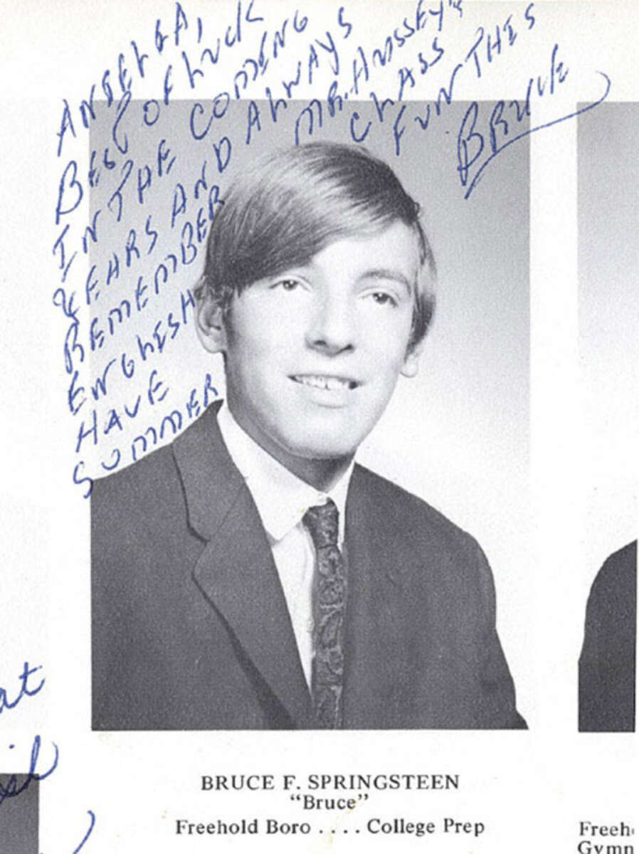 Black-and-white high school yearbook photo of a young Bruce Springsteen in a suit and tie. A handwritten message in blue ink is written diagonally across the upper left and center of the image.