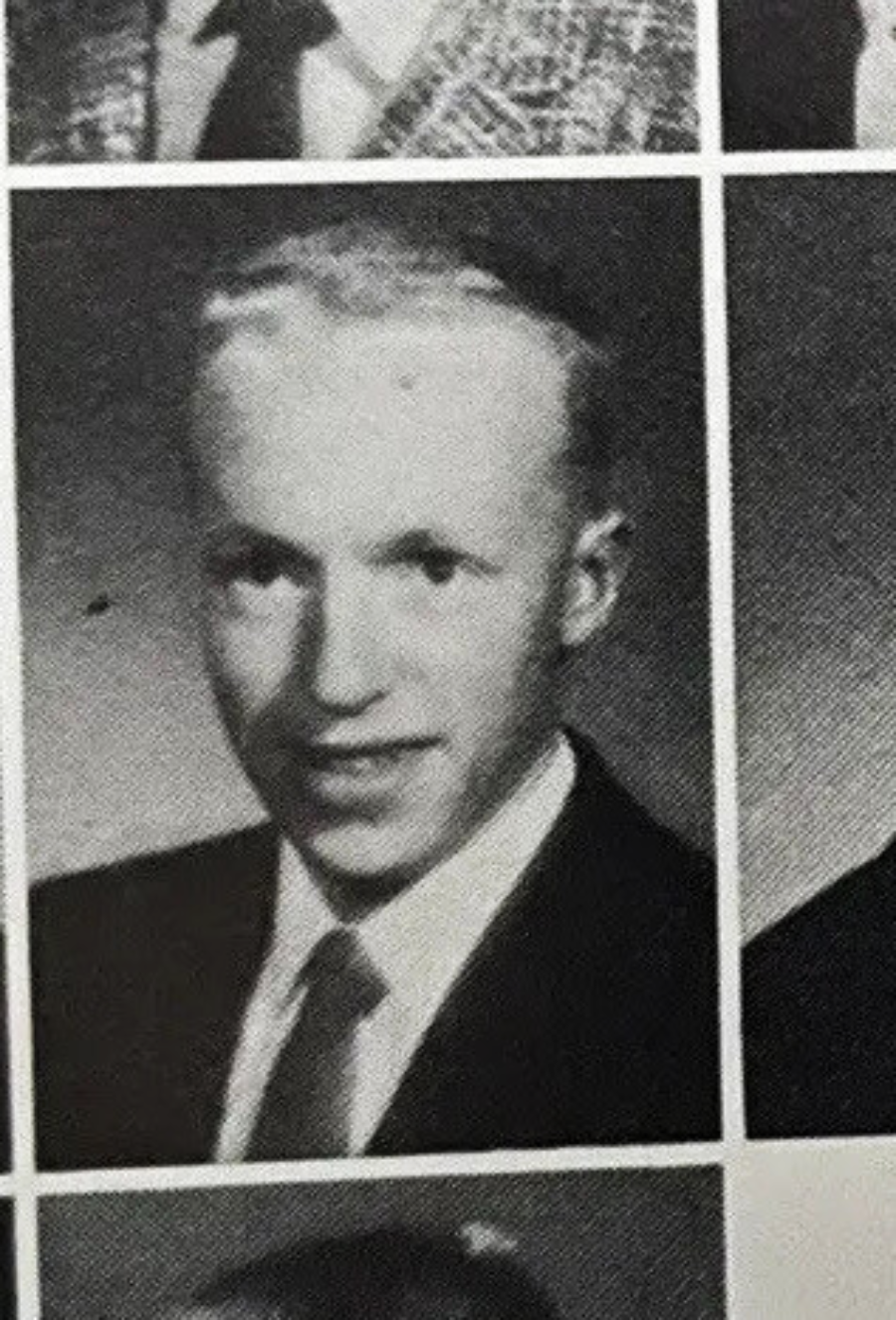 Black and white yearbook photo of a young man in a suit and tie, facing the camera and smiling slightly, with short hair and a plain background.