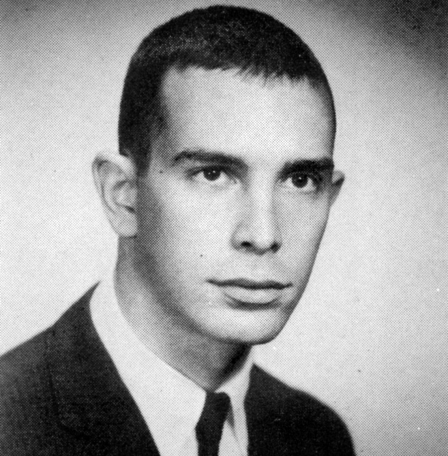 Black and white portrait of a young man with short dark hair, wearing a suit and tie, looking slightly to the side with a neutral expression against a plain background.