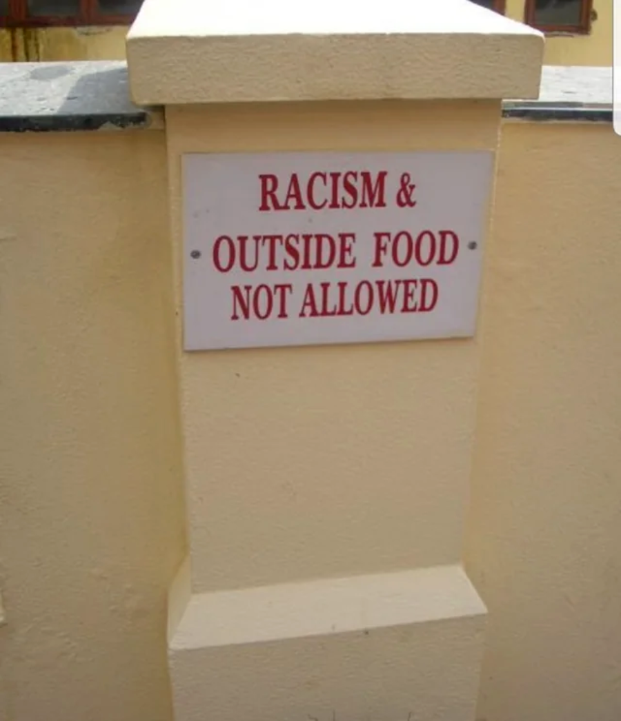A sign on a beige wall reads, "RACISM & OUTSIDE FOOD NOT ALLOWED" in red uppercase letters.
