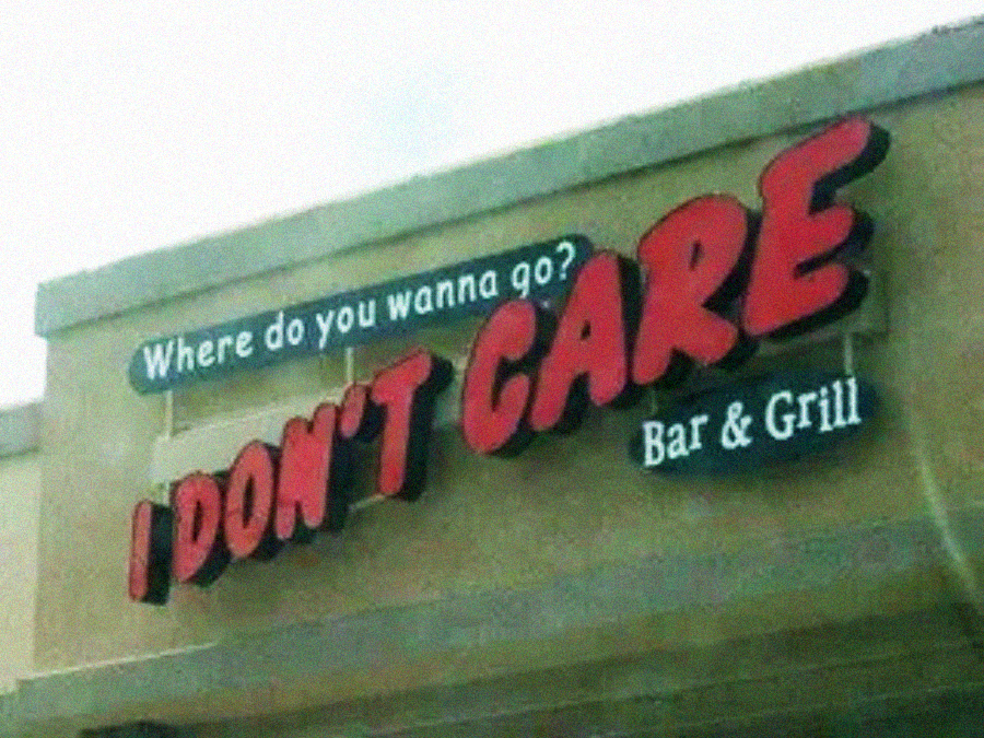 A restaurant sign reads, “Where do you wanna go? I DON’T CARE Bar & Grill,” with “I DON’T CARE” written in large, bold red letters and the rest in white on a tan building.