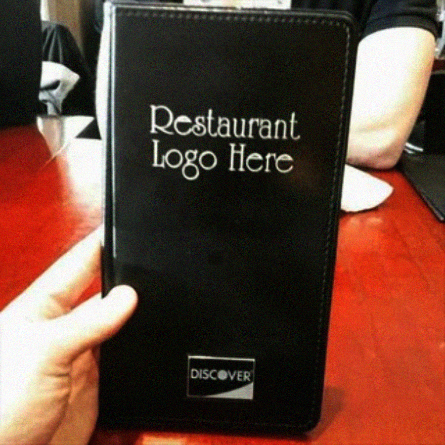 A person holds a black restaurant check presenter that reads "Restaurant Logo Here" and shows a Discover card slot, while seated at a wooden table.