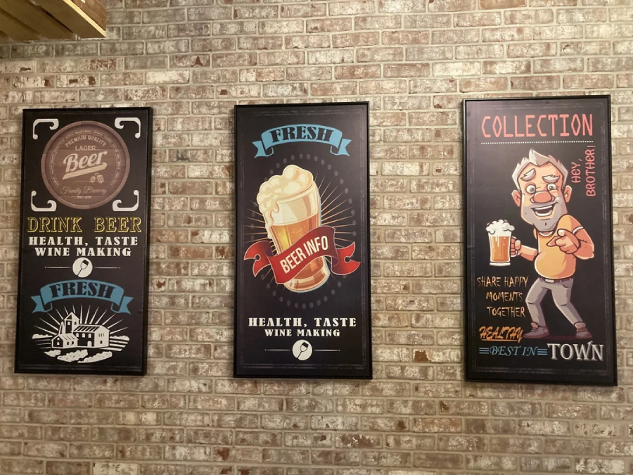 Three decorative posters on a brick wall, featuring beer-themed art and text about beer, health, taste, and sharing happy moments, with illustrations of beer glasses and a cheerful man holding a mug.