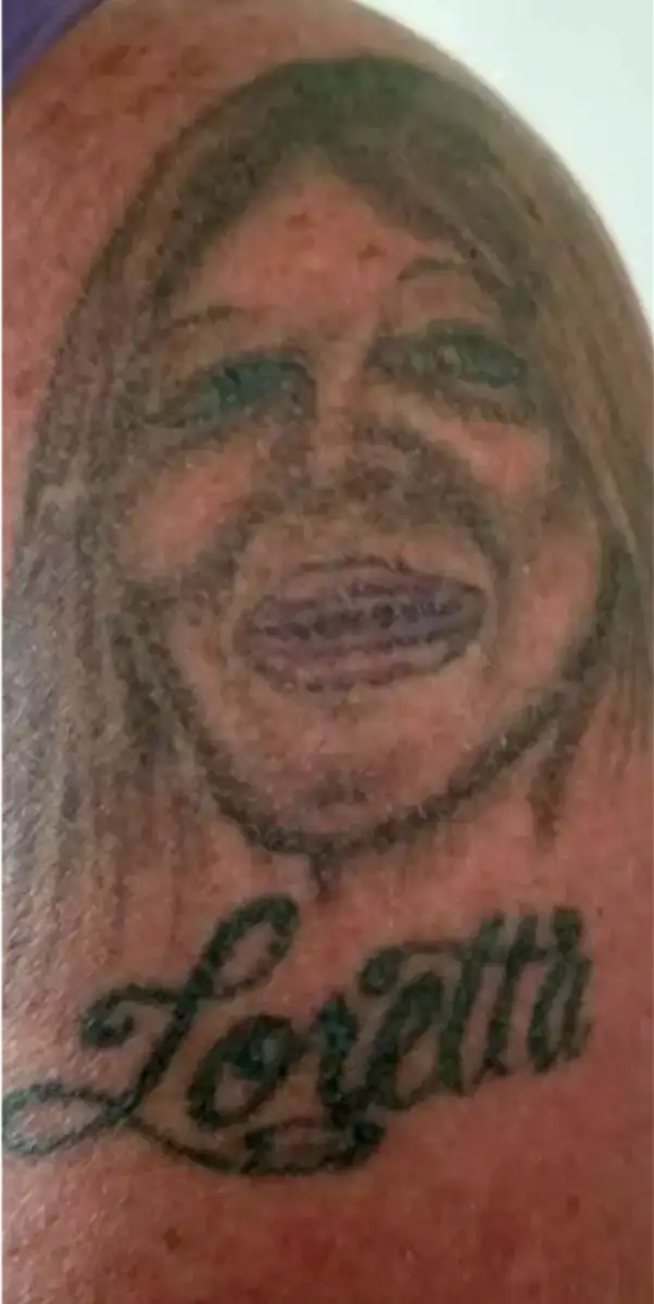 A tattoo of a woman's face with exaggerated features is inked above the name "Loretta" written in cursive on someone's skin.