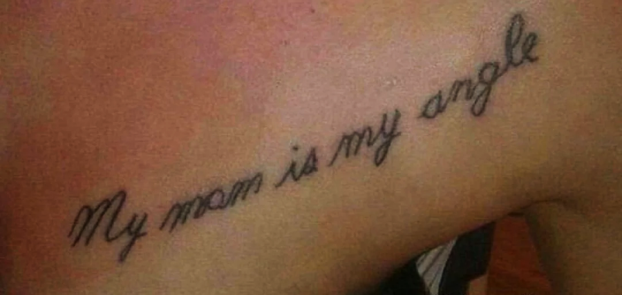 A tattoo in cursive script on someone’s skin reads, “My mom is my angle,” with a spelling error; “angle” is written instead of “angel.”