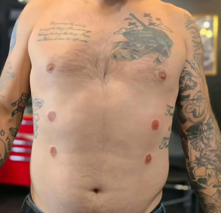 A shirtless person with multiple tattoos on their chest and arms, and four additional artificial nipples tattooed on their torso, two on each side of their natural nipples.