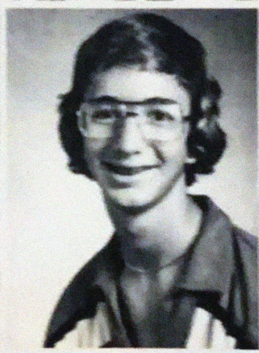 A black and white yearbook-style portrait of a young person with medium-length hair, wearing glasses and a collared shirt, smiling at the camera.