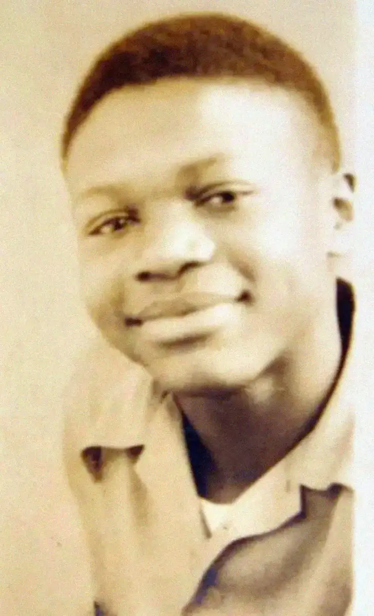 A sepia-toned portrait of a young person with short, neatly styled hair, wearing a collared shirt and smiling softly at the camera.