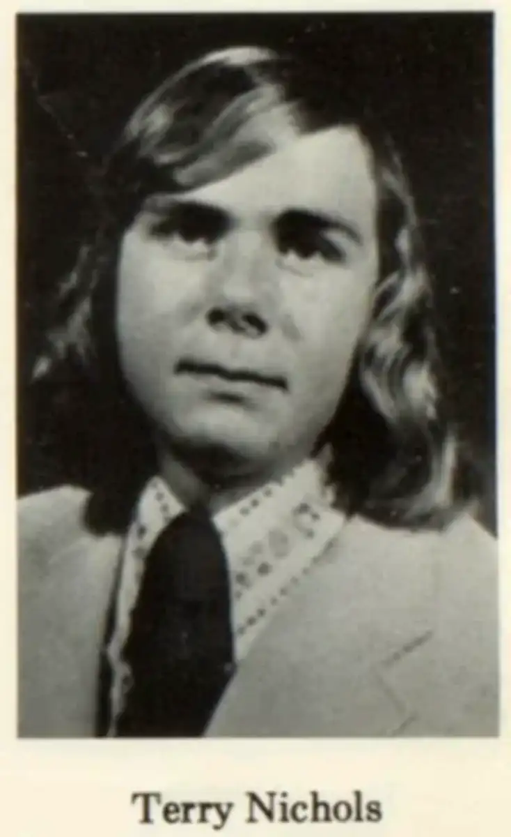 A young man with shoulder-length, wavy hair wearing a light-colored suit jacket, a patterned dress shirt, and a dark tie. He is looking at the camera with a neutral expression. The name "Terry Nichols" appears below.