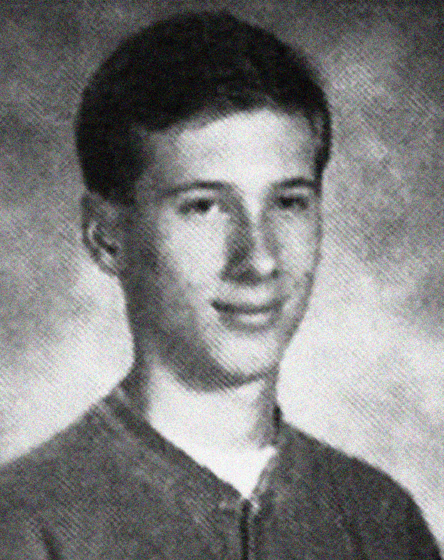 A black and white yearbook-style portrait of a teenage boy with short dark hair, wearing a light-colored shirt and looking slightly to the side with a neutral expression. The background is a textured gray.