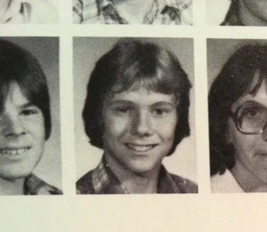 A black-and-white yearbook page shows three teenage students’ portraits. The student in the center has medium-length hair, is smiling, and wears a plaid shirt. The other two students are partially visible.