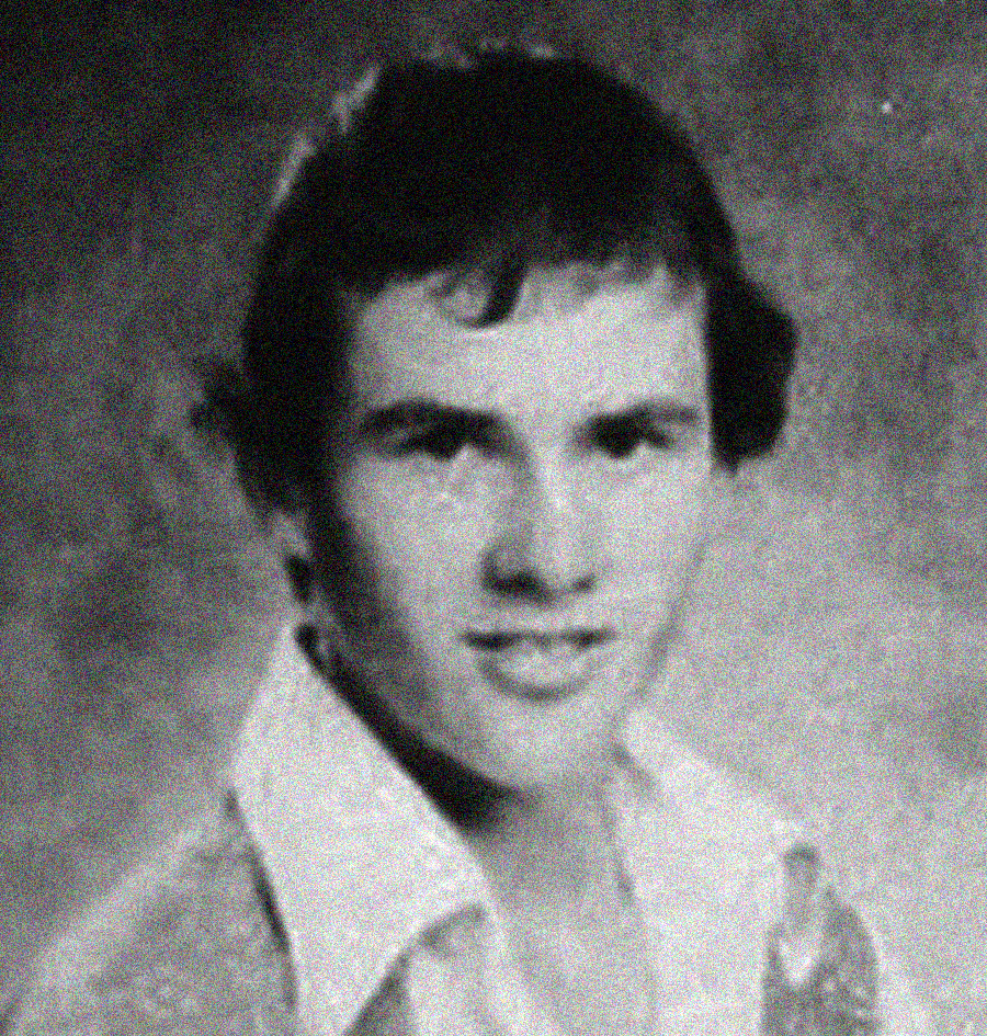 A black and white, vintage-style portrait of a young man with short, dark hair, wearing a collared shirt and a sweater. The background is plain and softly blurred.