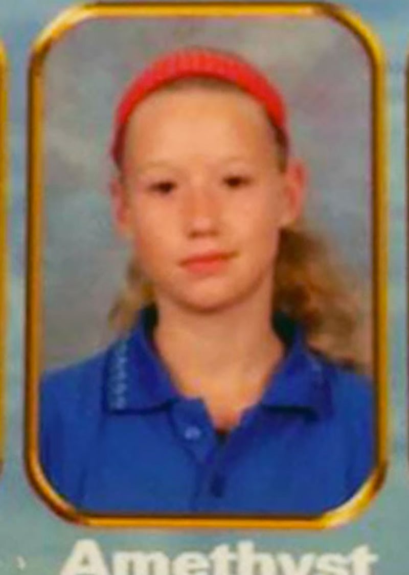 A school portrait of a young person with light skin, long blonde hair, wearing a red headband and a blue collared shirt, looking directly at the camera with a neutral expression.