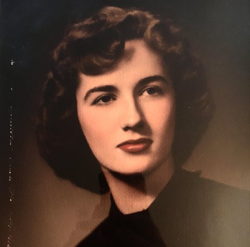 A vintage portrait of a woman with short, wavy brown hair, wearing a dark top, looking slightly to the side with a calm expression against a dark background.