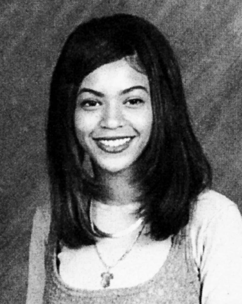 A black-and-white portrait of a young woman with straight, shoulder-length hair, wearing a light-colored top over a shirt and a necklace, smiling at the camera against a plain background.