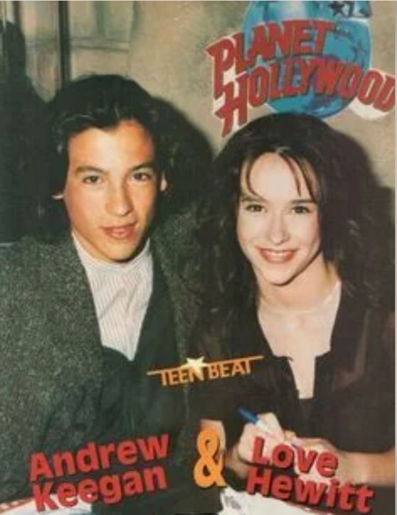 Two young celebrities smile together in front of a Planet Hollywood sign. The names "Andrew Keegan" and "Love Hewitt" appear in red and yellow text, along with the Teen Beat logo at the bottom.