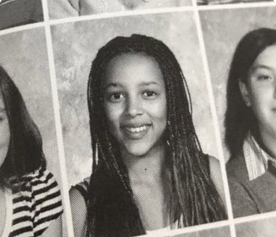 Black and white yearbook photo of a young person with long braided hair, smiling at the camera, centered between two other partially visible portraits.