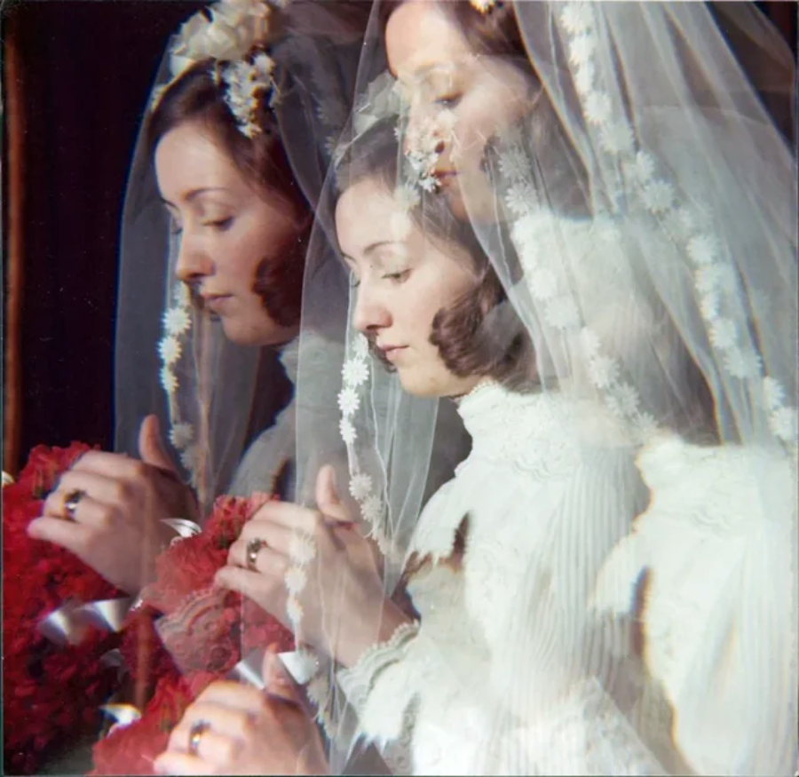 A bride in a white lace wedding dress and veil holds a bouquet of red flowers. The image has a double exposure effect, showing overlapping, translucent versions of her face and hands.