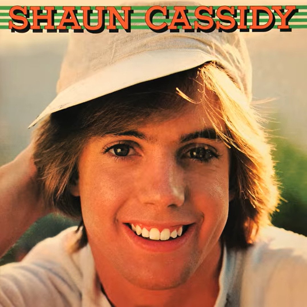 A young man with light brown hair smiles at the camera while wearing a white cap. The background is softly blurred. The text "SHAUN CASSIDY" appears at the top in large orange and green letters.