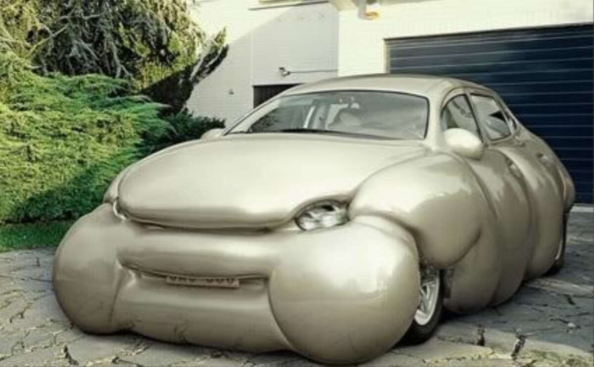 A beige car is parked on a driveway, but its exterior appears unusually bloated and puffy, as if inflated, giving it an exaggerated and distorted look. The background includes greenery and a garage door.