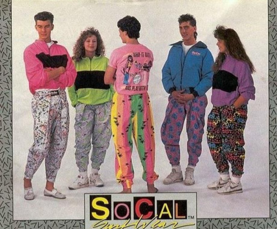 Five people wearing colorful, patterned 1980s outfits with baggy pants, windbreakers, and sneakers, standing together and smiling. The background has a retro design and the text “SoCal Surf Wear” at the bottom.