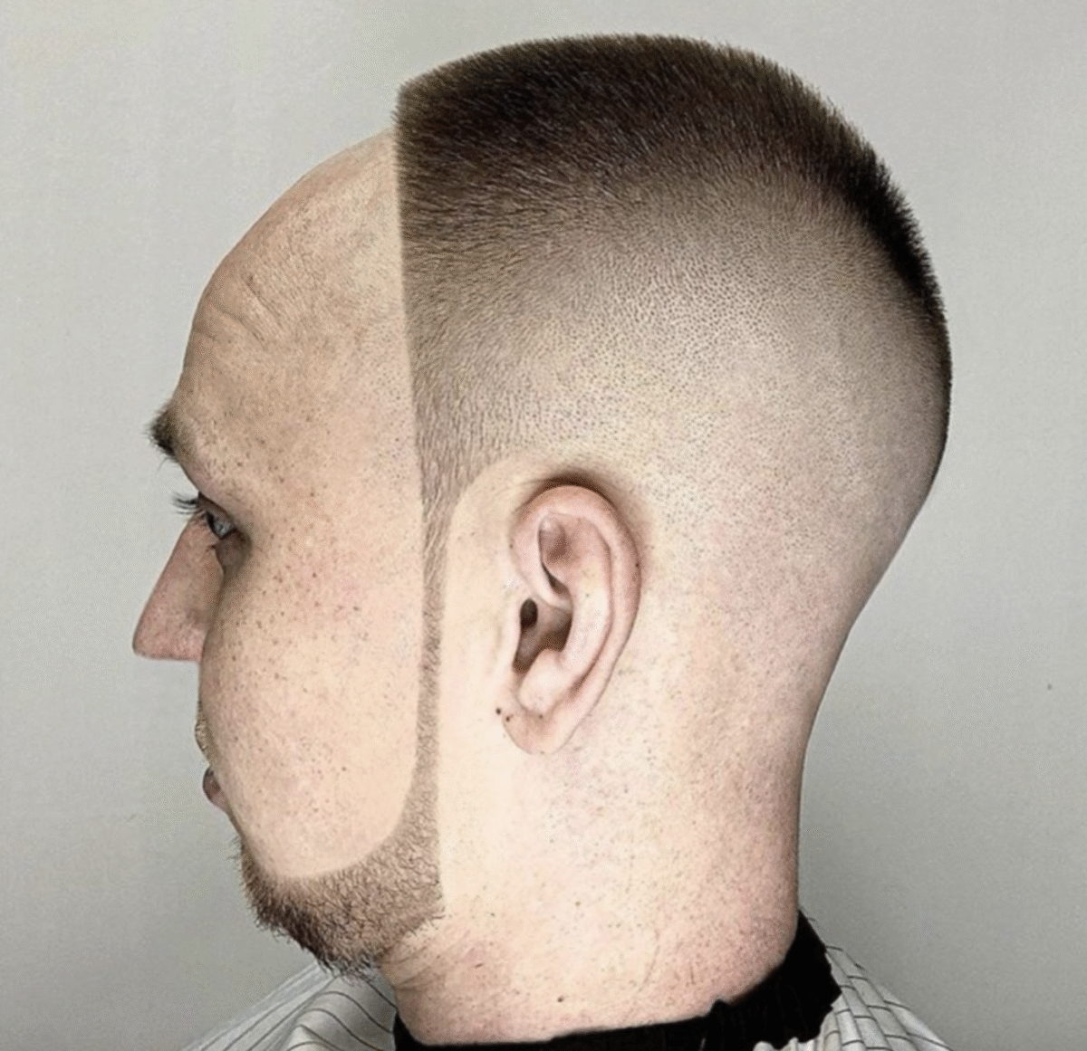 A man with a unique haircut: the left side of his head has a shaved geometric line dividing a bald side from a short buzz cut side, creating a dramatic visual contrast.