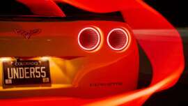 Close-up of the rear of a yellow Corvette with glowing red taillights, Colorado license plate reading "UNDERS5," and red light trails swirling around the car at night.