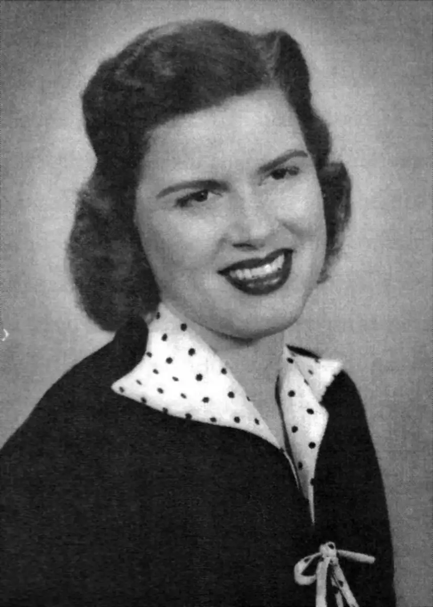 Black-and-white portrait of a smiling woman with wavy dark hair, wearing a polka-dot collared blouse and a dark jacket with a bow at the neckline, facing slightly to the side.
