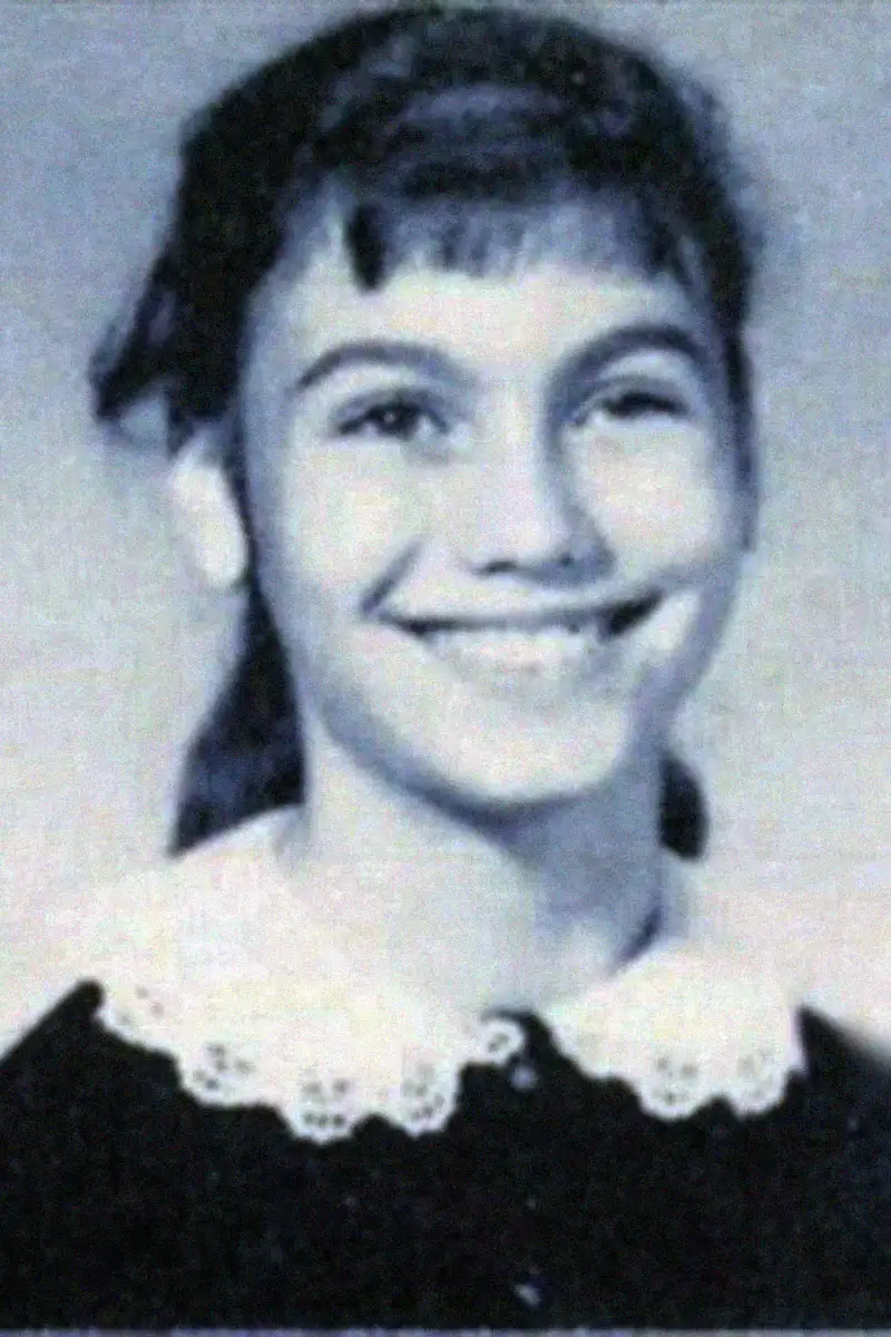 Black-and-white yearbook-style photo of a smiling young girl with dark hair in a ponytail, wearing a dress with a white lace collar.