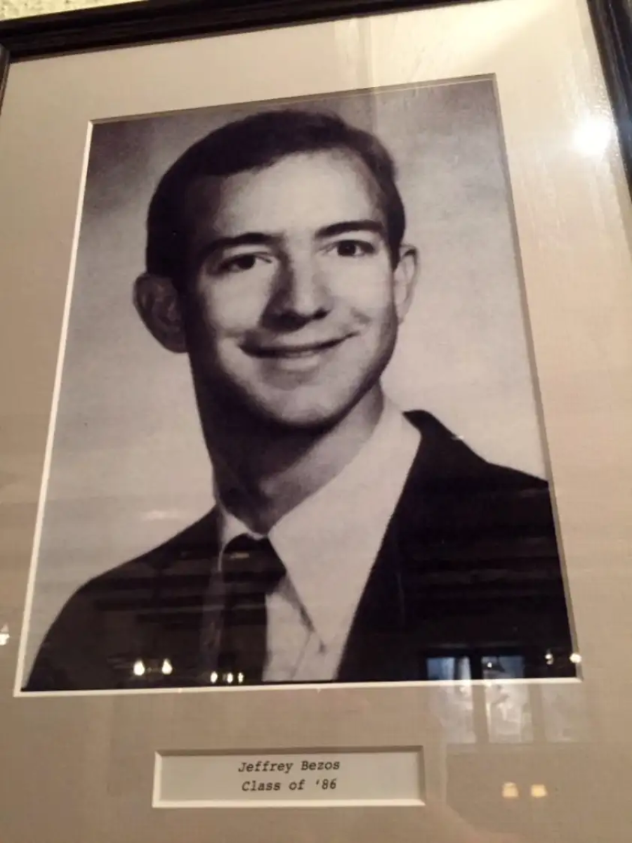 A framed black-and-white portrait of a young man in a suit and tie, smiling at the camera. A plaque below the photo reads “Jeffrey Bezos, Class of ‘86.”