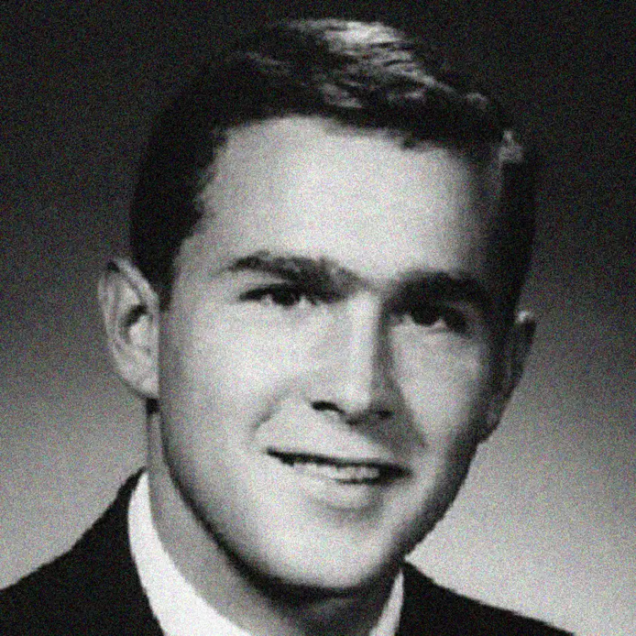 Black and white portrait of a young man with short, neatly combed hair, wearing a suit and tie, smiling slightly while looking at the camera. The background is plain and dark.