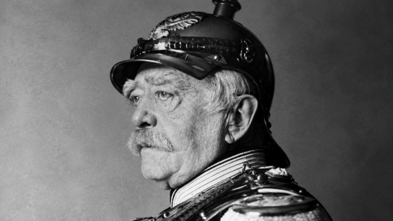 Elderly man in profile wearing a decorated military helmet and uniform, with a mustache and serious expression, against a plain background.