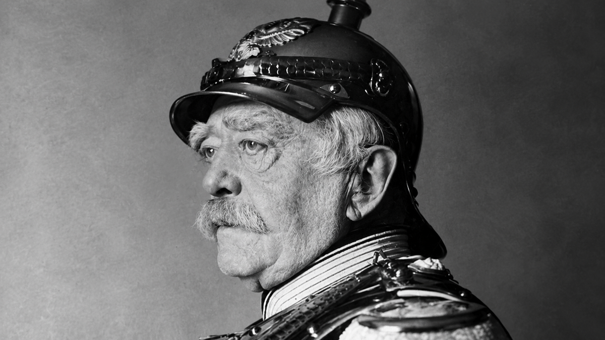 Elderly man in profile wearing a decorated military helmet and uniform, with a mustache and serious expression, against a plain background.