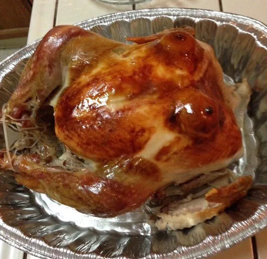 A roasted turkey in a disposable aluminum pan, with two round, shiny spots on the breast resembling human breasts, giving the bird a humorous appearance.