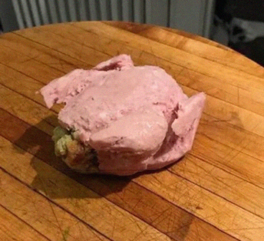 A whole cooked chicken coated in a thick layer of pink paste sits on a round wooden cutting board with visible grooves.