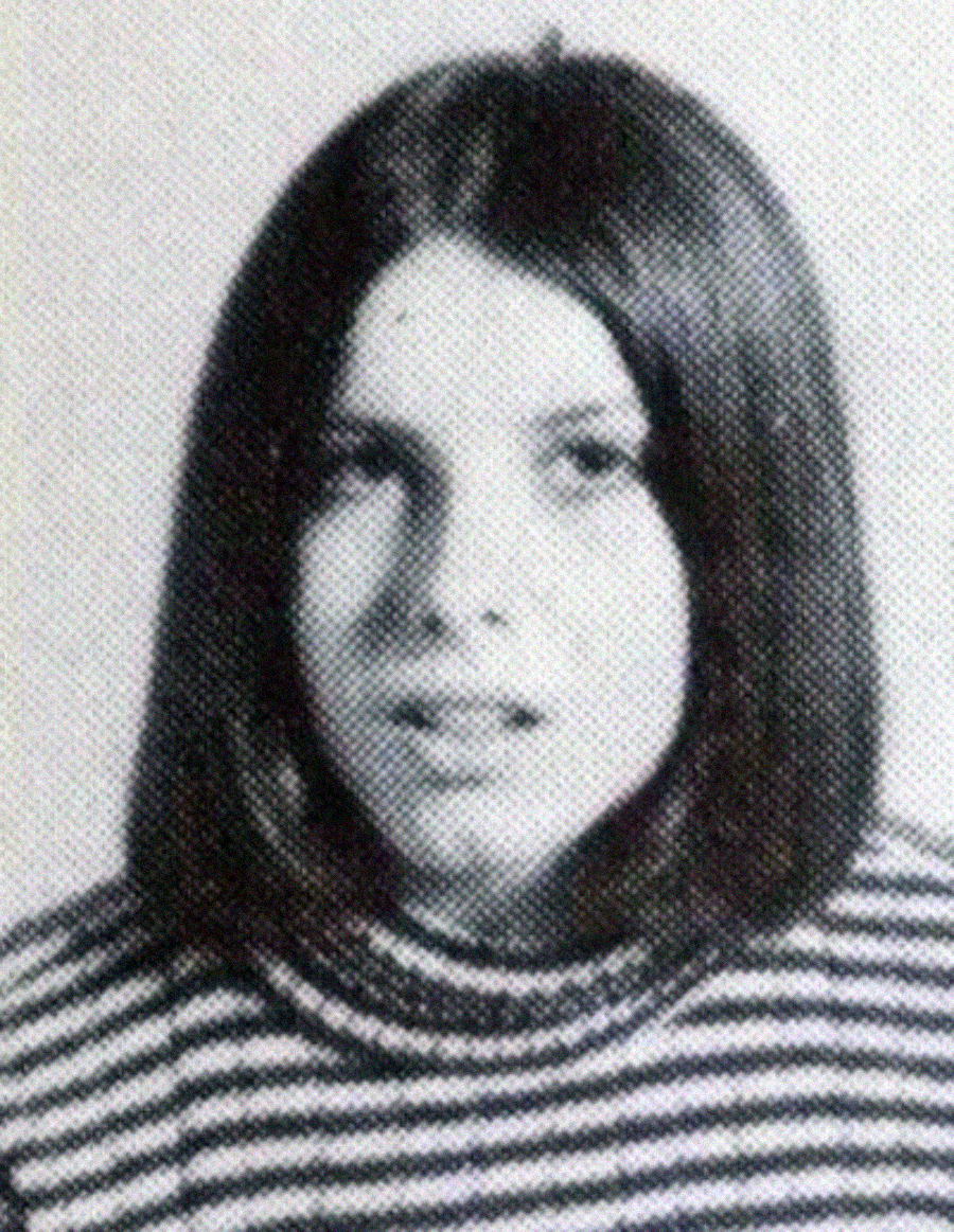 A black and white portrait of a young person with straight, medium-length dark hair, wearing a striped turtleneck shirt, looking slightly past the camera with a neutral expression.