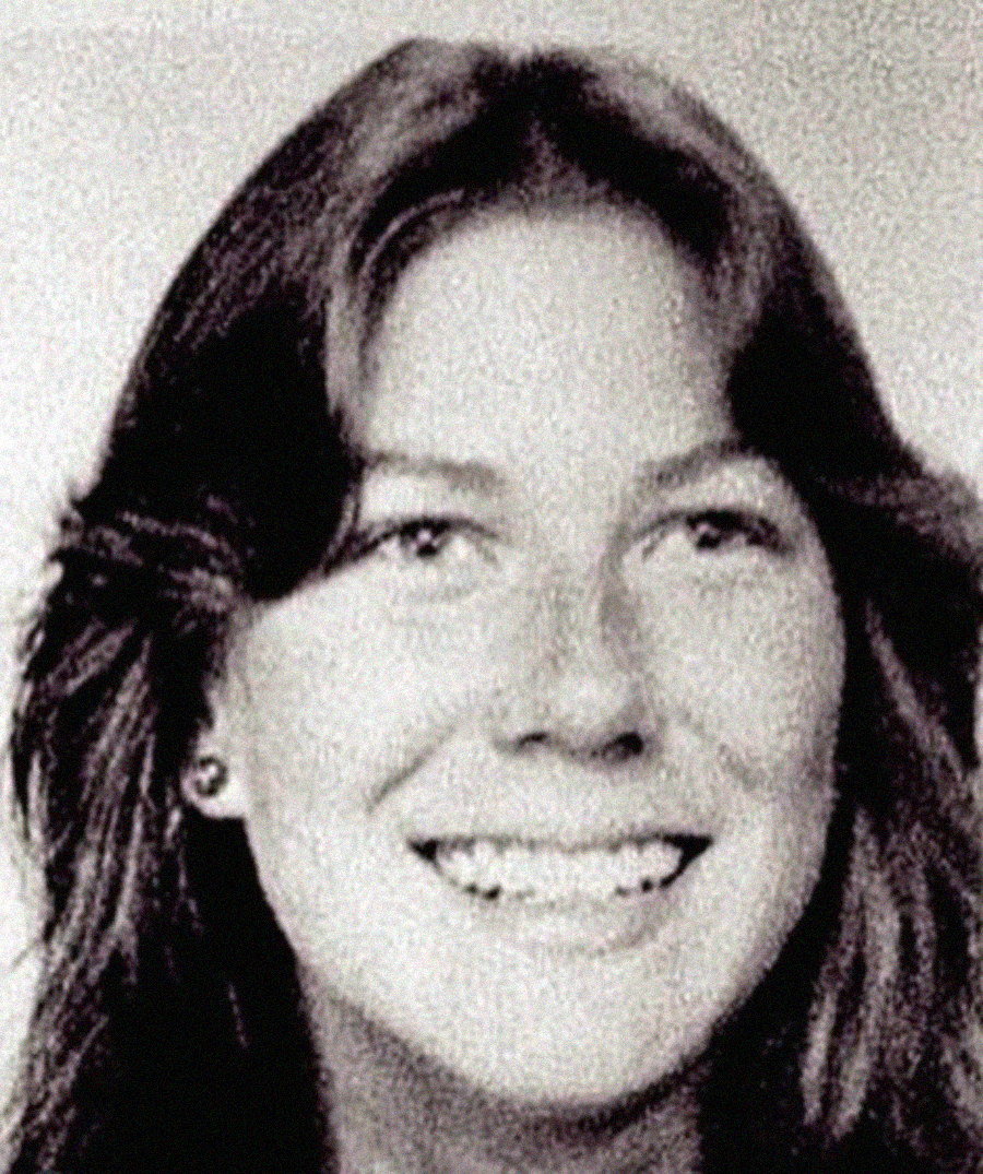 Black-and-white portrait of a young woman with long hair, smiling and looking slightly to the side. She is wearing a light-colored top and small earrings. The photo has a grainy texture.
