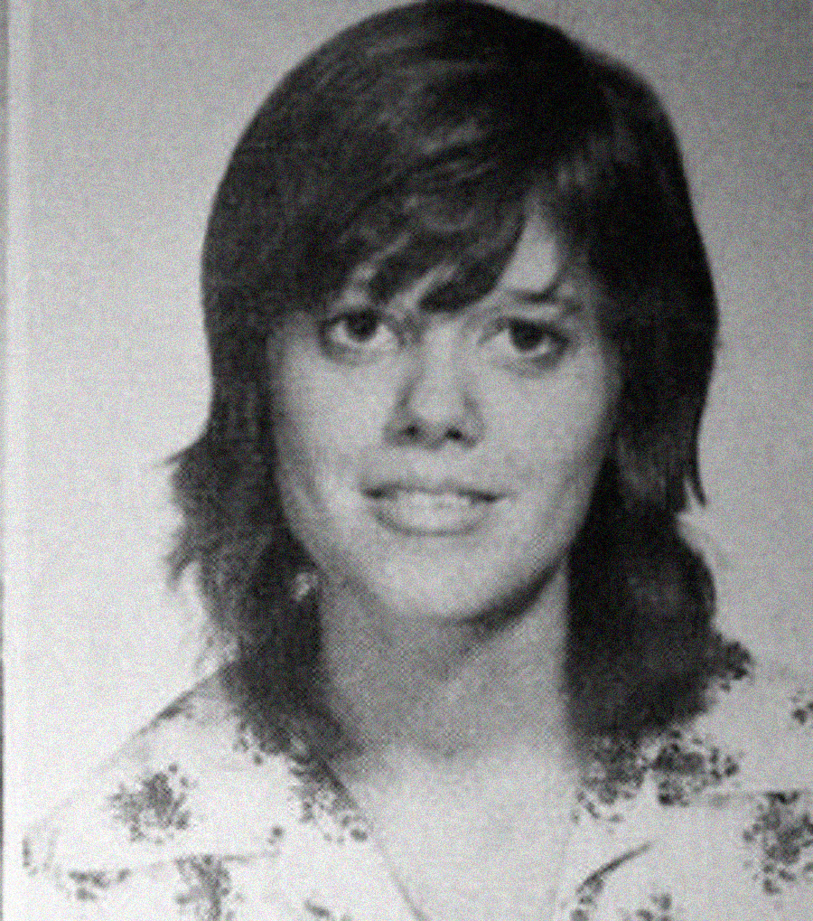 Black and white portrait of a young woman with medium-length hair, wearing a patterned shirt, looking at the camera and smiling slightly.