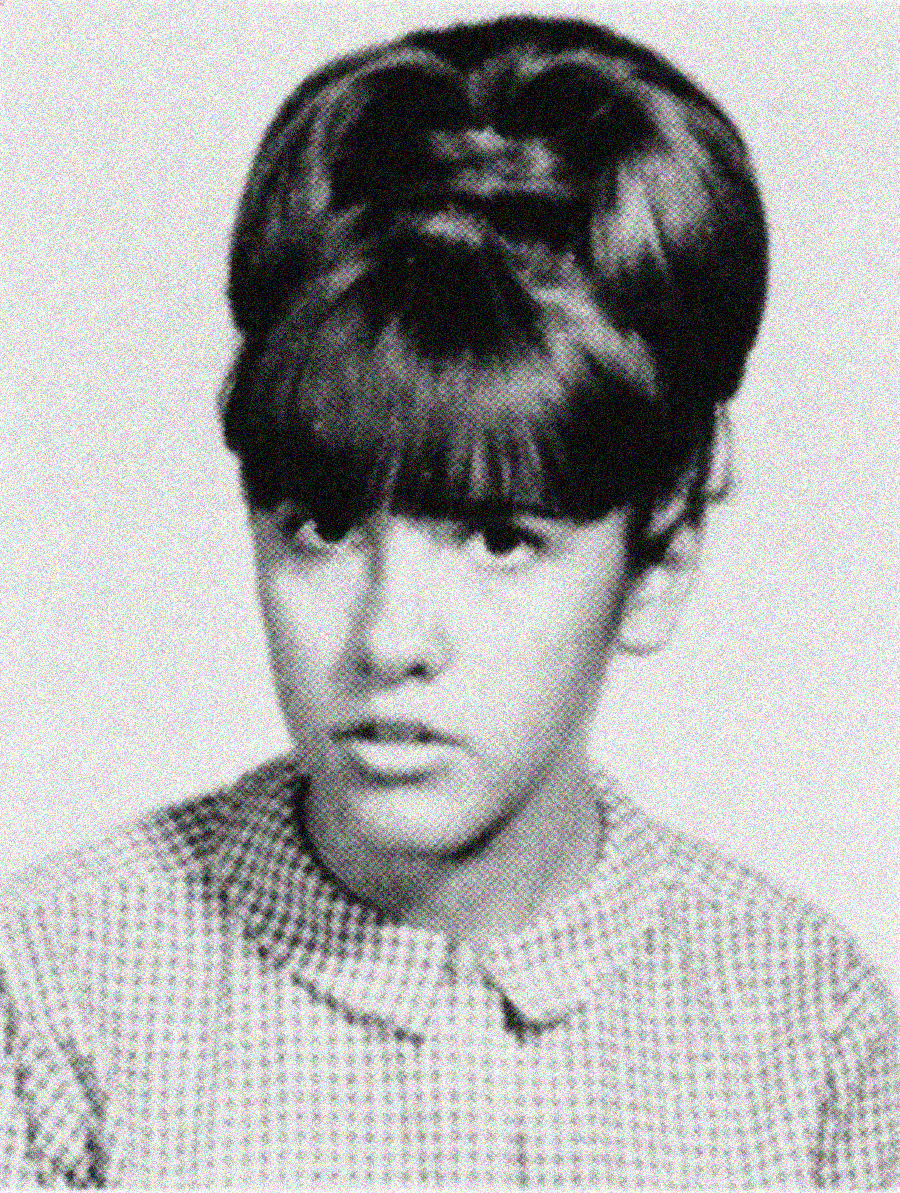 Black and white portrait of a young girl with dark, voluminous hair and bangs, wearing a patterned, buttoned-up top. She faces forward with a neutral expression.