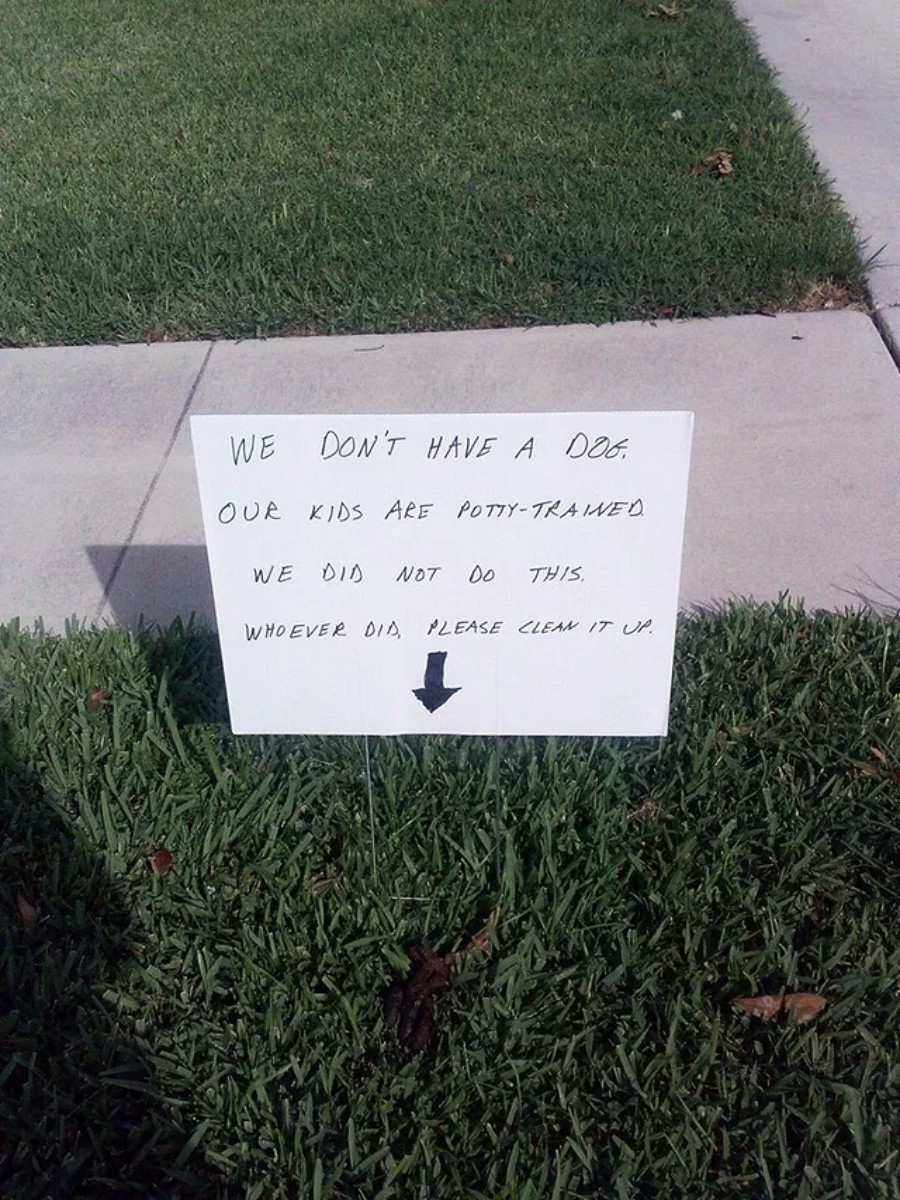 A handwritten sign on grass reads: "We don't have a dog. Our kids are potty-trained. We did not do this. Whoever did, please clean it up." An arrow points to the ground below.