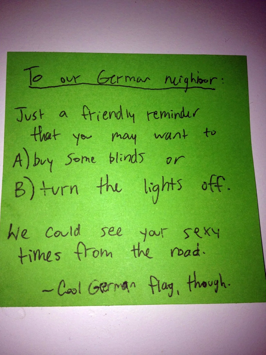 A green sticky note with a handwritten message reminding a German neighbor to buy blinds or turn off their lights, as people can see their private moments from the road. It ends with, "Cool German flag, though.