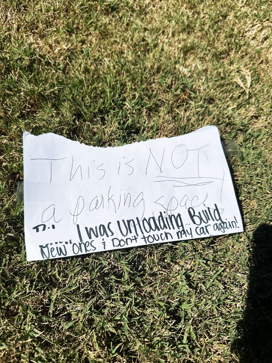 A handwritten note on grass reads: "This is NOT a parking space! I was unloading. Build new ones & don't touch my car again.