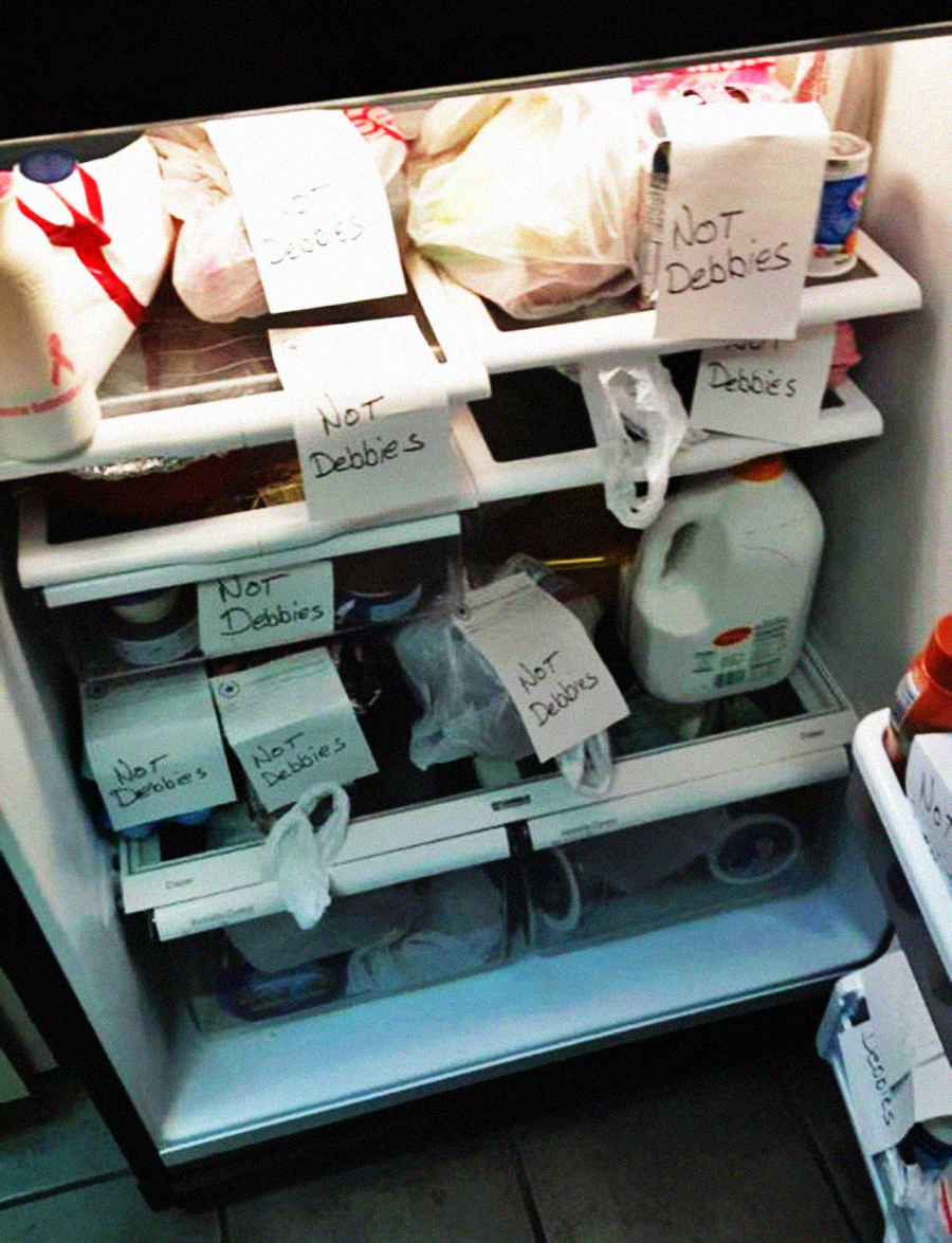 An open refrigerator with several items on the shelves, each labeled with handwritten notes saying "Not Debbie's." The fridge contains milk, containers, bags, and a few boxes with the same label.